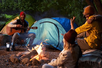 winter night of group of friends gathered around bonfire playing guitar singing outdoors. multiracial people sitting together enjoying camping in nature. positive relationships and healthy getaways.