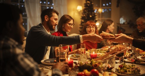 portrait with parents, children and friends enjoying christmas dinner together in a cozy home in the evening. relatives sharing meals, singing traditional festive songs and setting off fireworks