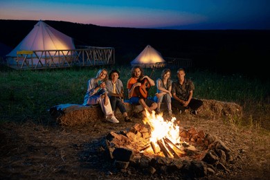 charismatic and attractive happy group of friends have a good time at the campsite they singing playing on the guitar while sitting down on the haystack beside the fire stake