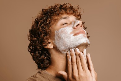 handsome man enjoying beauty treatment while applying face cream and standing on brown background