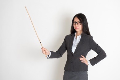 asian female teacher angry and holding a stick, standing on plain background.