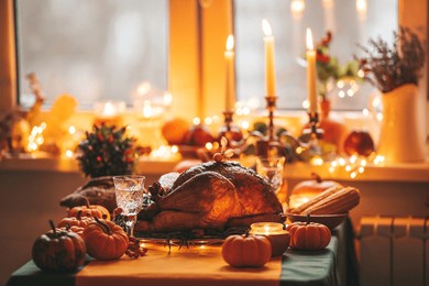 thanksgiving day dinner with holiday autumn decor and candles. family dining room table set with delicious golden roasted turkey on platter garnished rosemary fresh small pumpkins