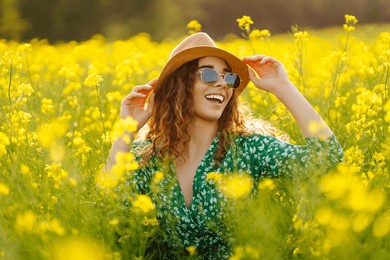 a happy woman in a hat walks through a blooming rapeseed field. beautiful woman posing in a rapeseed field on a sunny day. concept of nature, relaxation.