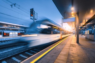blurred high speed train on the modern railway station at night in graz, austria. fast moving intercity passenger train on the railway platform at sunset. railroad. passenger railway transportation