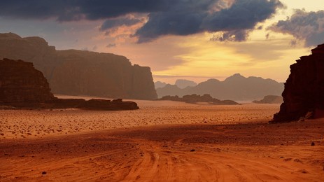 sunset over a desert with rock formations and scattered clouds. dramatic sky. panoramic wallpaper of wadi rum desert, jordan.
