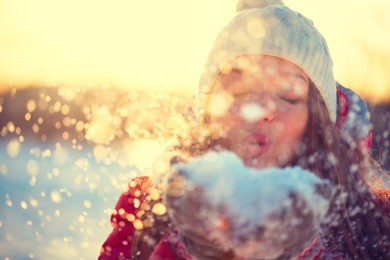 beauty winter girl blowing snow in frosty winter park. outdoors. flying snowflakes. sunny day. backlit. joyful beauty young woman having fun in winter park. defocused