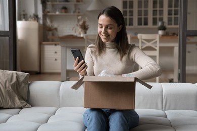 pretty woman sit on sofa opens received courier parcel box, reviewing order in retail services using app on smart phone, check items feels happy with delivered goods. e-commerce client, tech concept