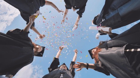 happy graduates throwing up colorful confetti against the blue summer sky.