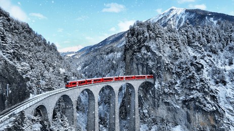 snow falling and train passing through famous mountain in filisur, switzerland. train express in swiss alps snow winter scenery. 