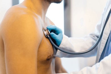 an unrecognizable doctor uses a stethoscope on the chest of an adult patient to diagnose heart-related pathologies. a man visits a doctor's office. auscultation.profile view of a medical center.