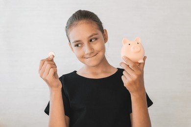 happy excited teen girl saving money, dropping coin into pink piggy bank, cheerful female teenager enjoying economy, investing finances for suture, standing over grey studio background, copy space
