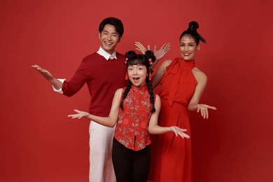 happy asian family wearing red costume presenting or showing open hand palm with copy space for product isolated on red background. present product advertising concept.