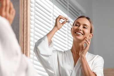beautiful woman applying cosmetic serum onto her face near mirror in bathroom