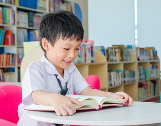 asian boy student in uniform reading book in school library