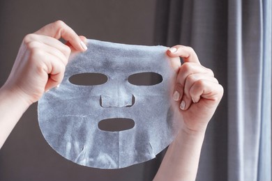 female hands with white manicure hold fabric mask on gray background.