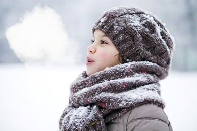 close-up portrait of a little girl in brown jacket and knit scarf and hat on a background of a snow park