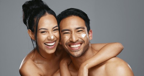 couple, smile and love for skincare, care and portrait with moisturizer in studio by gray background. happy people, dermatology and hug for cosmetics, hydration and creme or love for skin treatment
