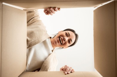 surprised young asian woman unpacking. opening carton box and looking inside. packaging box, delivery service. human emotions and facial expression