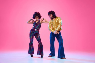 talented dancers, man and woman in retro style outfits posing against gradient pink studio background. concept of american culture, 1970s, 1980s fashion, music, comparisons of eras.
