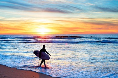 surfer with surfboard walking on the beach at sunset