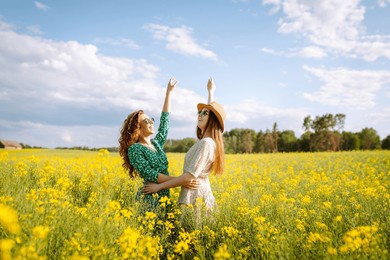 smiling female tourists walking through flowering field, touching yellow flowers. nature, vacation, relax and lifestyle. summer landscape.