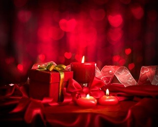 valentine's day. valentine red heart shaped candles and gift on red silk over glowing background. beautiful valentine card art design