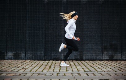side view of sporty young woman running on sidewalk in morning. health conscious concept with copy space.