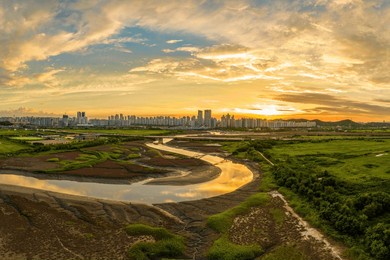 aerial and sunset view of misaeng bridge on tidal channel and mud flat with waterway against bangsan bridge and apartments at bangsan-dong near siheung-si, south korea
