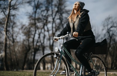 a female cyclist with her eyes closed takes a moment to enjoy the peaceful atmosphere of a park on a sunny day.