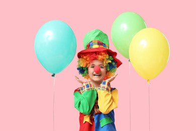 funny little boy in clown costume with balloons on pink background. april fools day celebration