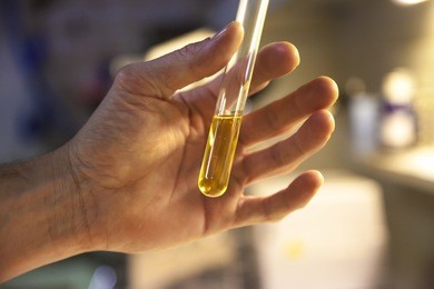 scientist hand holding a test tube with a yellow aqueous solution 