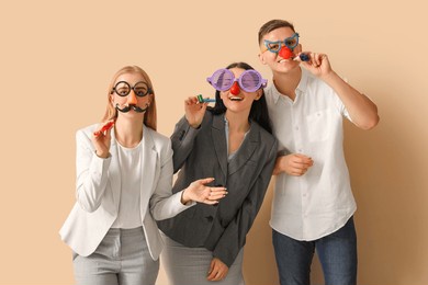 business people in funny disguise with party whistles on beige background. april fools' day celebration