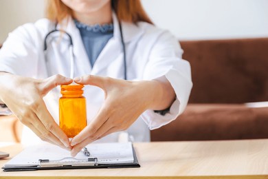 doctor's hand shows heart shape, records health examination results and medication usage of patient, pill bottle, healthcare, and medical checkup concept.