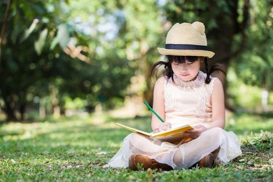little asian girl use pencil writing on notebook for writing book with smiling face in the park