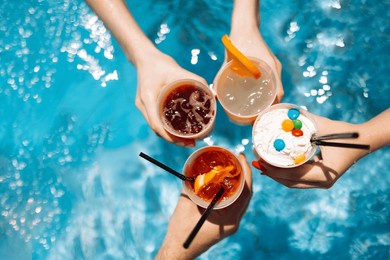 close-up of female and male hands holding glasses with iced cocktails and clinking them. friends make festive toast with delicious drinks against background of clear blue pool water. party, vacation.