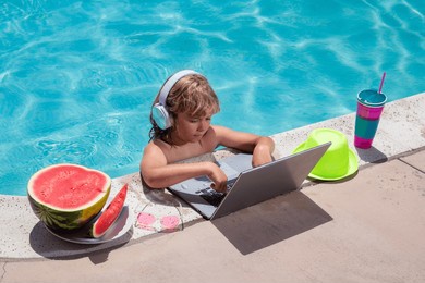 child working with laptop on summer vacation holidays. little freelancer using computer, remote working in swimming pool. summer online technology.