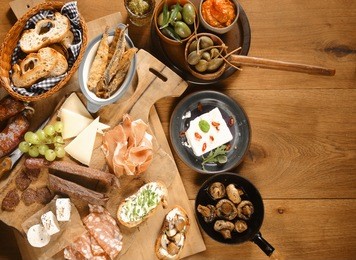 high angle shot of various freshly made mouth watering appetizers and snacks on wooden board and plates on top of wooden table