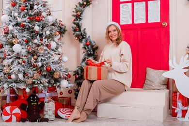 a young woman in a santa hat with a gift in her hands sits on the porch next to the christmas tree.