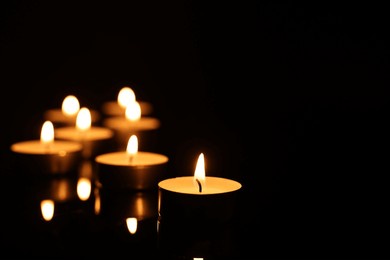 burning candles on mirror surface in darkness, closeup. space for text