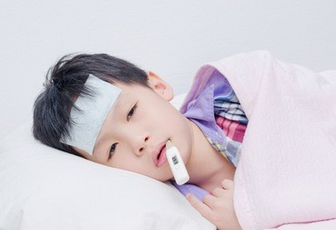 little sick boy lying on bed with digital thermometer in mouth