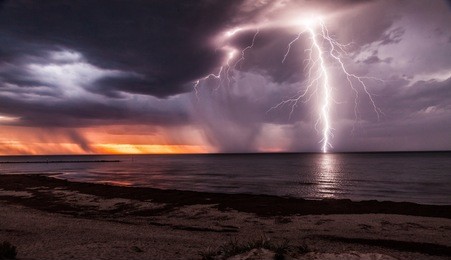 lightening storm moving in over beach at sunset.