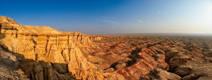 panorama over the rock formations and cliffs of the so-called "white stupa", a mountainous primeval landscape in the gobi desert, mongolia in the warm light of the rising or setting sun