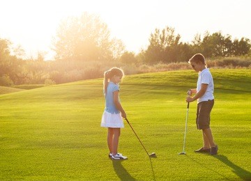 casual kids at a golf field holding golf clubs. sunset