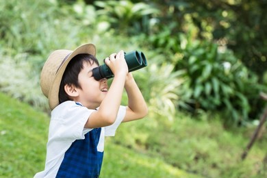 little asian boy looking trough a binoculars with smiling face in park