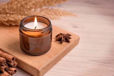 massage scented burning candle in amber glass jar, winter hygge home interior decor on wooden tray with cinnamon sticks and anise, copy space. soy wax eco candle.