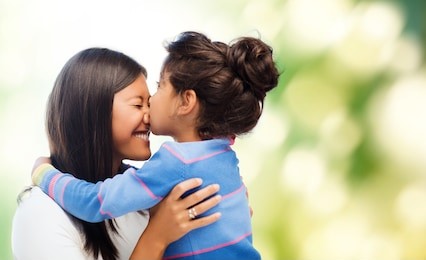 family, children and happy people concept - happy little girl hugging and kissing her mother over green background