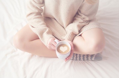 legs of girl warm woolen socks and a cup of coffee warming, winter morning at home in bed