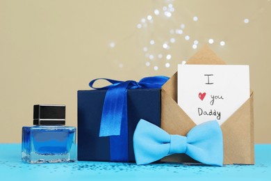 happy father's day. card with phrase i love you, daddy in envelope, bow tie, perfume and gift box on light blue table, closeup