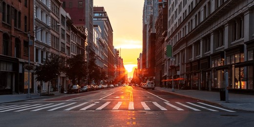 empty streets and sidewalks at 5th avenue and 23rd st in new york city with sunset shining between the buildings of the manhattan cityscape