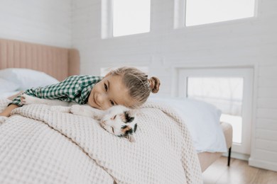 a little blond girl wearing pajamas hugs a domestic cat in her bedroom. the concept of a cozy home morning